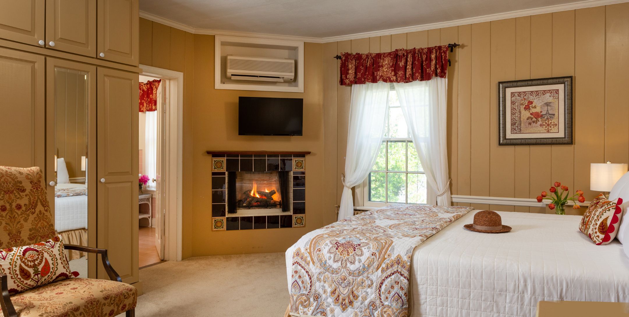 Paneled guest room with warm tones, carpeting and hardwood, corner fireplace, and storage.