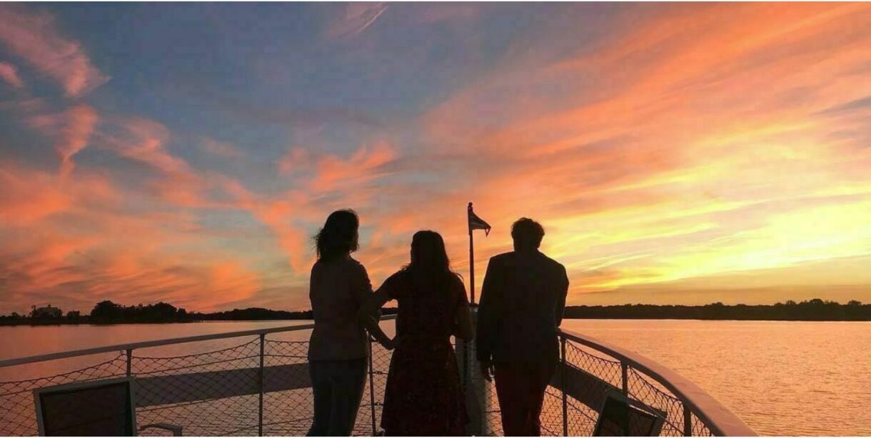 3 people on bow of boat watching the sunset.