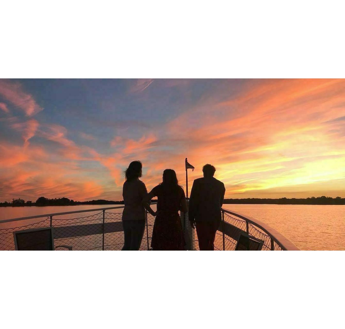 3 people on bow of boat watching the sunset.